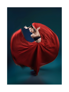 Eine Ballerina in einem roten Rock tanzt elegant vor einem dunklen Hintergrund.