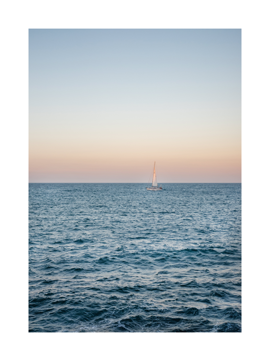 Fotografie eines Segelboots auf dem Meer bei Sonnenuntergang.