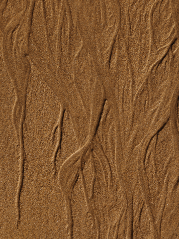 Nahaufnahme von Sand mit wellenförmigem Muster in Beige.