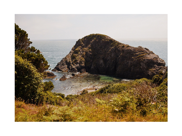 Fotografie von Felsen im Meer mit einem kleinen Strand im Vordergrund.