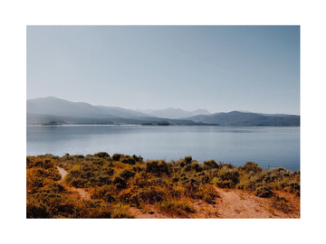 Landschaftsfotografie eines Sees mit Bergen im Hintergrund und Vegetation im Vordergrund.