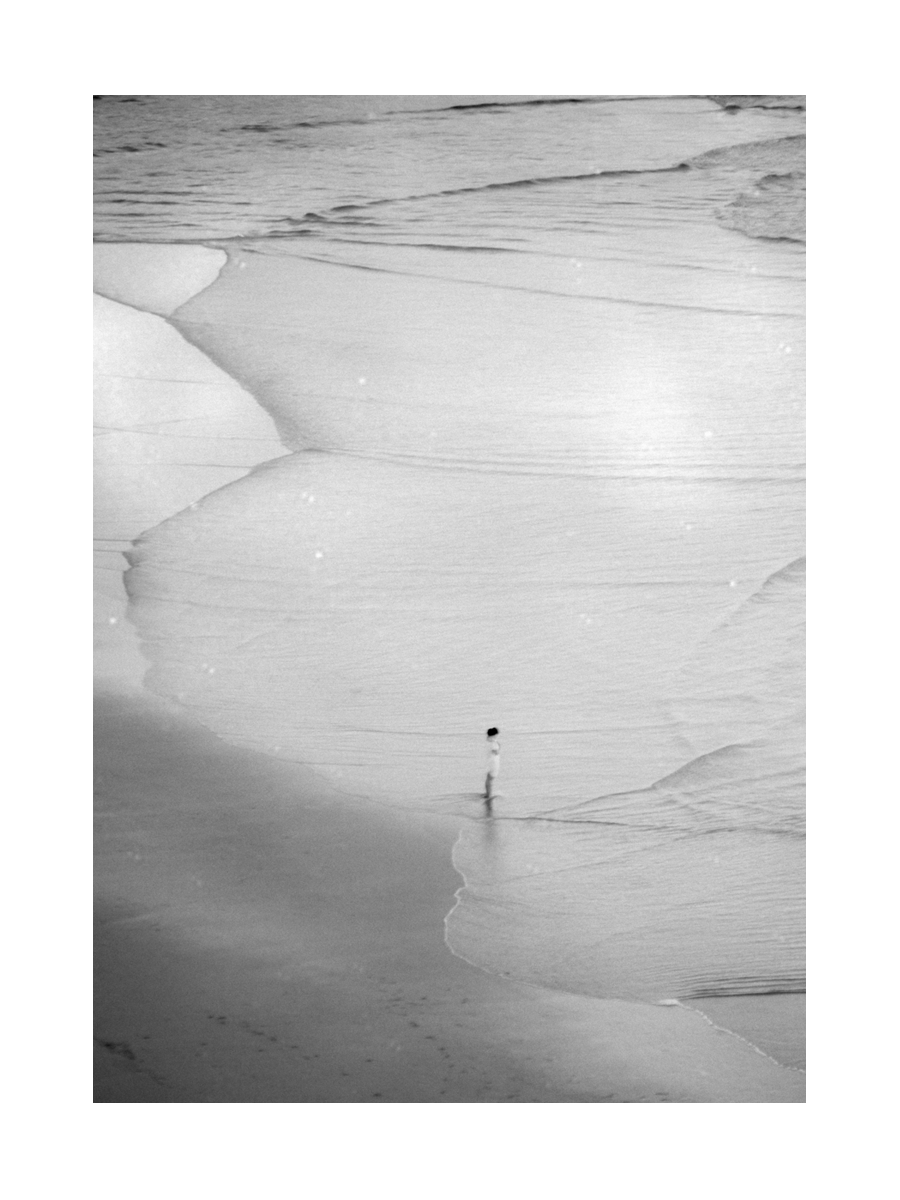 Schwarzweißfoto eines Mannes allein am Strand.