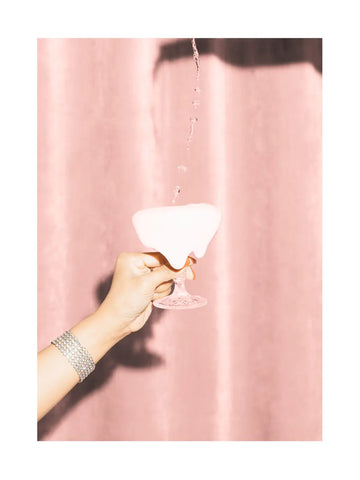 Hand hält ein Glas mit verschüttetem rosa Getränk vor rosa Hintergrund.
