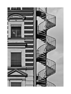 Schwarz-Weiß-Fotografie eines Gebäudes mit Wendeltreppe und einer Person im Fenster.