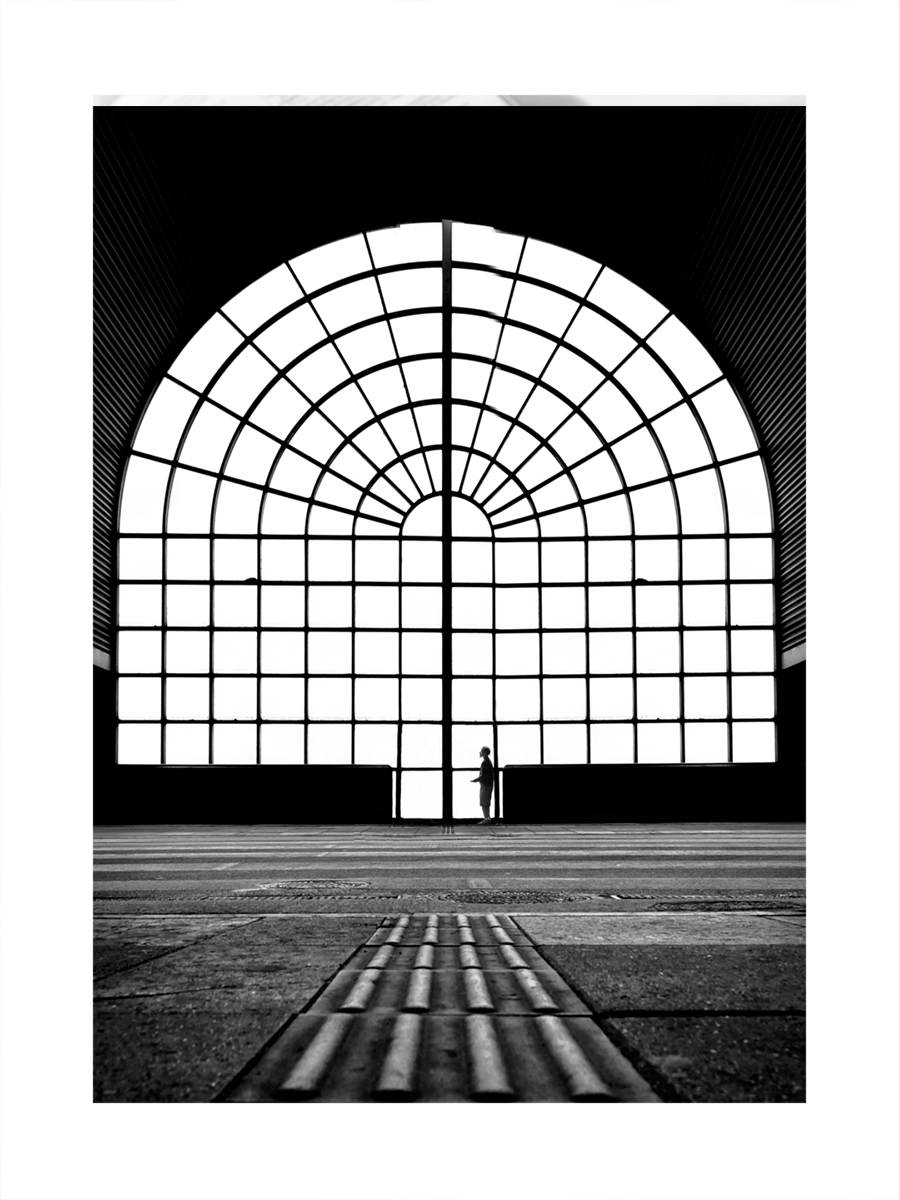 Schwarz-weiß-Fotografie eines großen Fensters mit quadratischen Scheiben und einer Person davor.