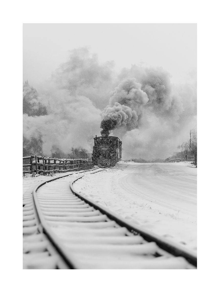 Schwarz-Weiß-Fotografie einer Dampflokomotive in einer verschneiten Landschaft.
