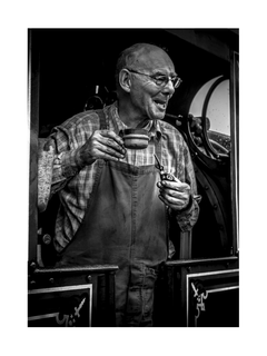 Schwarz-Weiß-Fotografie eines älteren Mannes in einer Lokomotive, der eine Tasse hält.