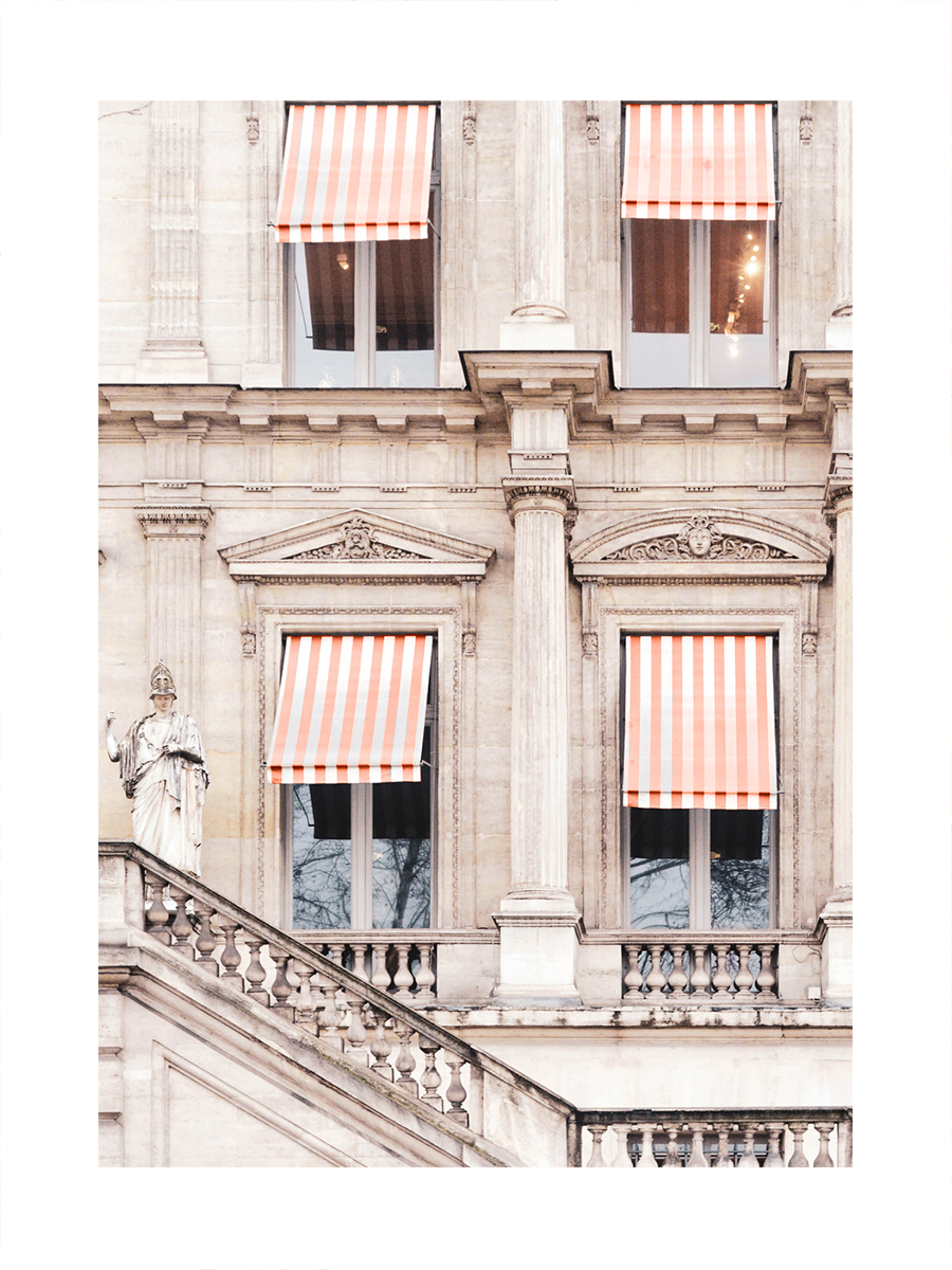 Fotografie einer beigen Hausfassade mit roten und weißen gestreiften Markisen über den Fenstern.
