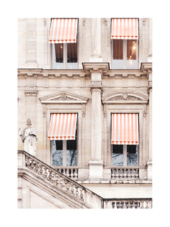 Fotografie einer beigen Hausfassade mit roten und weißen gestreiften Markisen über den Fenstern.