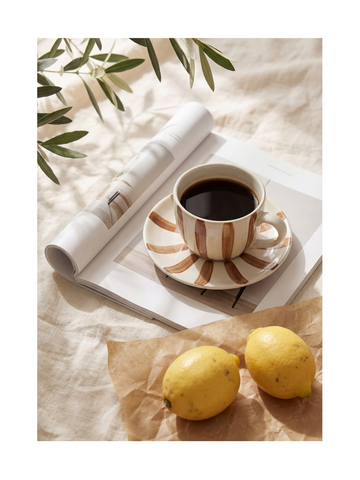 Gestreifte Kaffeetasse und Zitronen auf einem Tisch mit einer Zeitschrift im Hintergrund.