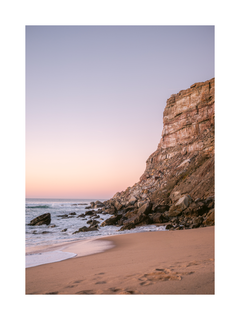 Fotografie eines Strandes mit einem großen Felsen und rosa Himmel.