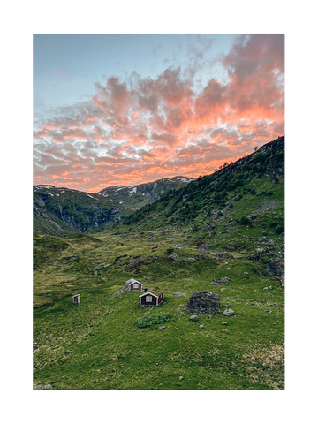 Landschaftsfoto mit grünen Hügeln, roten Häusern und einem orangefarbenen Himmel.