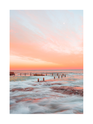 Sonnenuntergang am Meer mit Pfosten im Wasser und rosa Himmel.