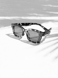 Schwarz-Weiß-Fotografie einer Sonnenbrille mit Wassertröpfchen auf einem Boden mit Palmenschatten.