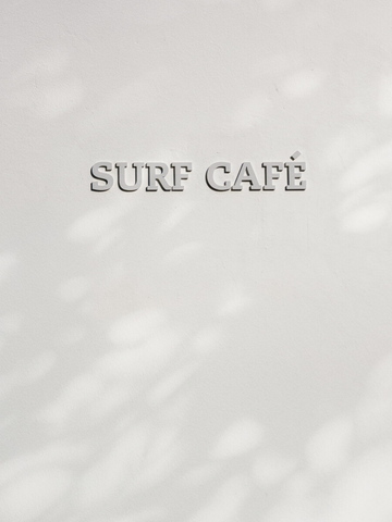 Fotografie des Schriftzugs "Surf Café" an einer weißen Wand mit Schatten.