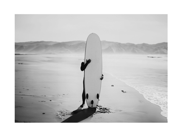 Schwarz-Weiß-Fotografie eines Surfers mit Surfbrett am Strand.