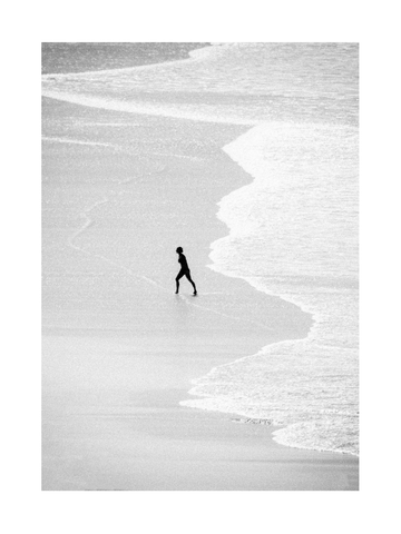 Schwarz-weiß-Fotografie eines Surfers, der am Strand entlanggeht.