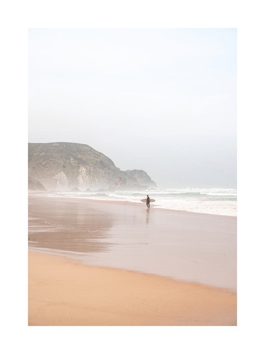 Fotografie eines Surfers am rosa Strand mit Wellen und einem Berg im Hintergrund.