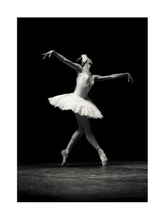 Schwarz-Weiß-Fotografie einer Ballerina in einem weißen Kleid auf der Bühne.
