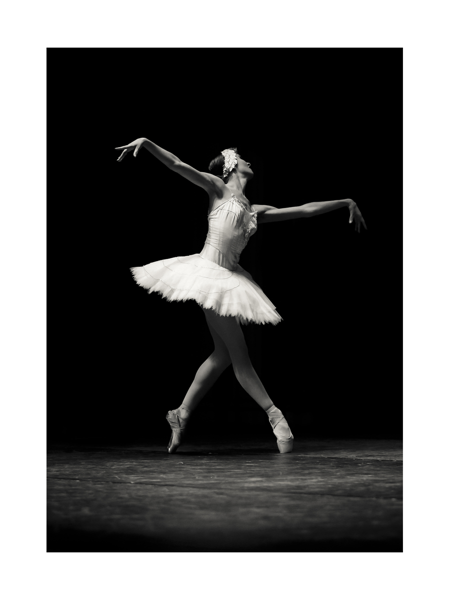 Schwarz-Weiß-Fotografie einer Ballerina in einem weißen Kleid auf der Bühne.