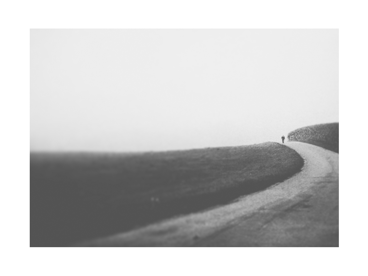 Schwarzweiß-Fotografie einer kurvigen Straße mit einer Figur im Hintergrund.