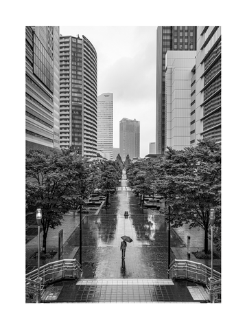 Schwarz-weiß-Fotografie einer Person mit Regenschirm zwischen hohen Gebäuden.