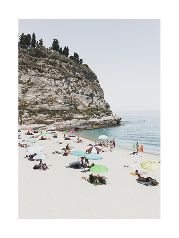 Fotografie eines Strandes mit bunten Sonnenschirmen und einem Felsen im Hintergrund.