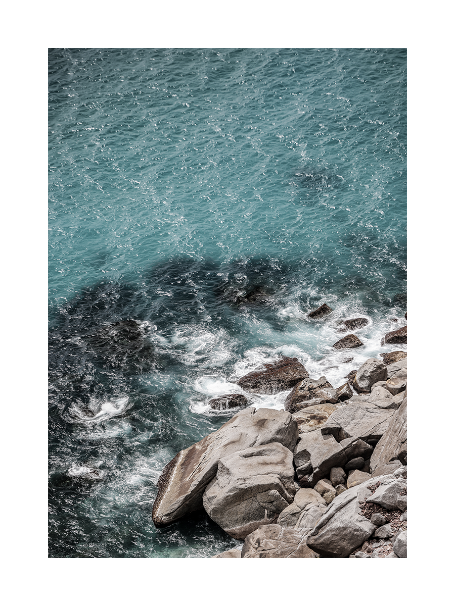 Fotografie von türkisfarbenen Wellen, die gegen Felsen schlagen.