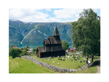 Fotografie der Stabkirche von Urnes in Norwegen mit umliegenden Bergen und Fjord.