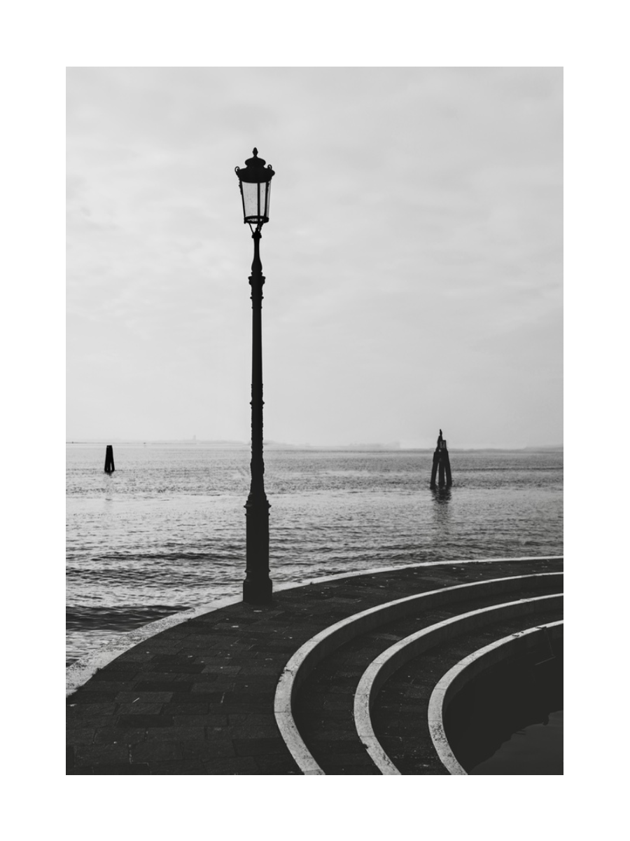 Schwarz-Weiß-Fotografie von Stufen und einer Straßenlaterne am Wasser in Venedig.