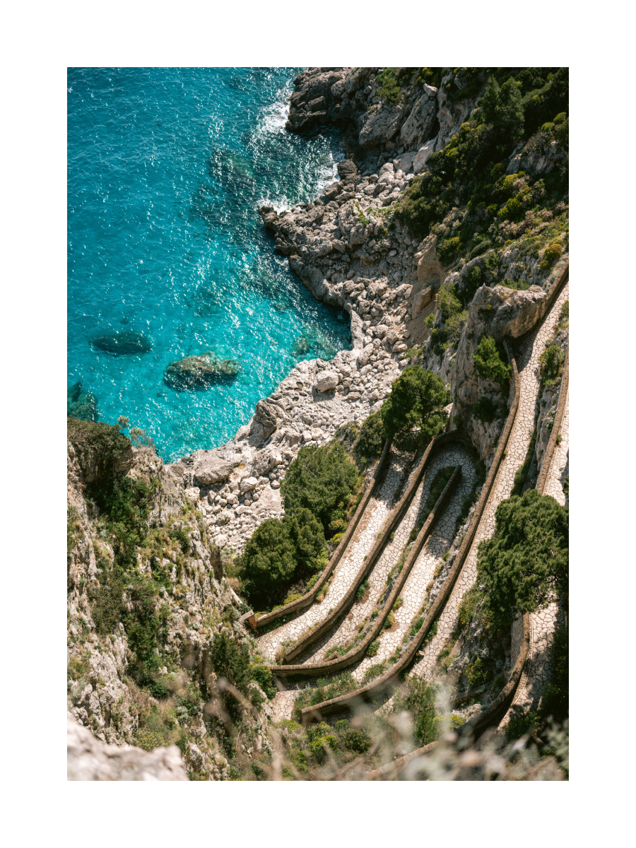 Fotografie der kurvigen Via Krupp auf Capri mit smaragdgrünem Wasser und üppigem Grün.