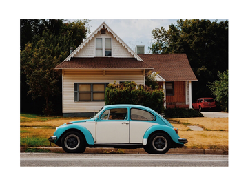 Fotografie eines türkisfarbenen Oldtimers vor einem Haus.