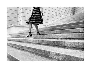 Schwarz-Weiß-Fotografie einer Frau in einem gestreiften Kleid, die eine Treppe hinuntergeht.