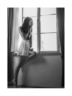 Schwarz-Weiß-Fotografie einer Frau in einem weißen Rock, die in einem Fenster sitzt.