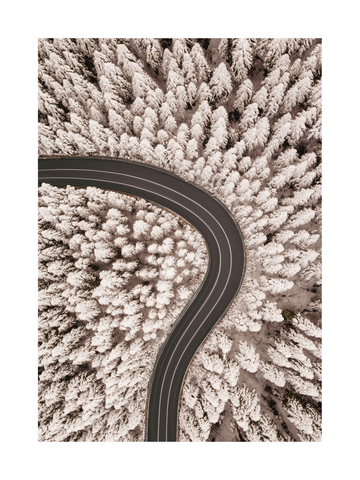 Luftaufnahme eines verschneiten Waldes mit einer kurvigen Straße in der Mitte.