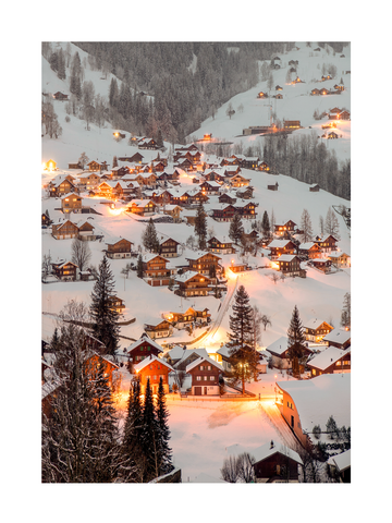 Verschneites Dorf mit warmen Lichtern und schneebedeckten Bäumen.