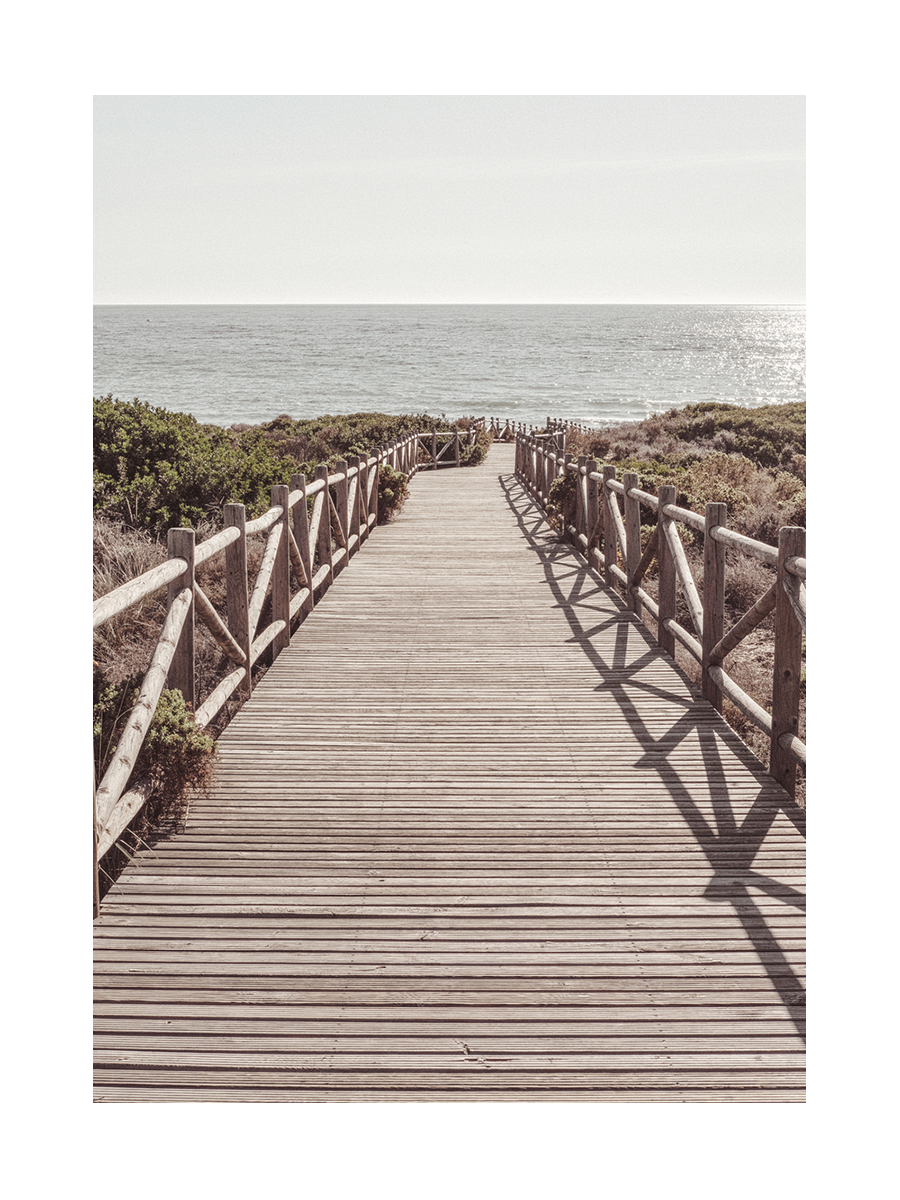 Fotografie eines Holzstegs, der zu einem Strand führt, mit dem Meer im Hintergrund.