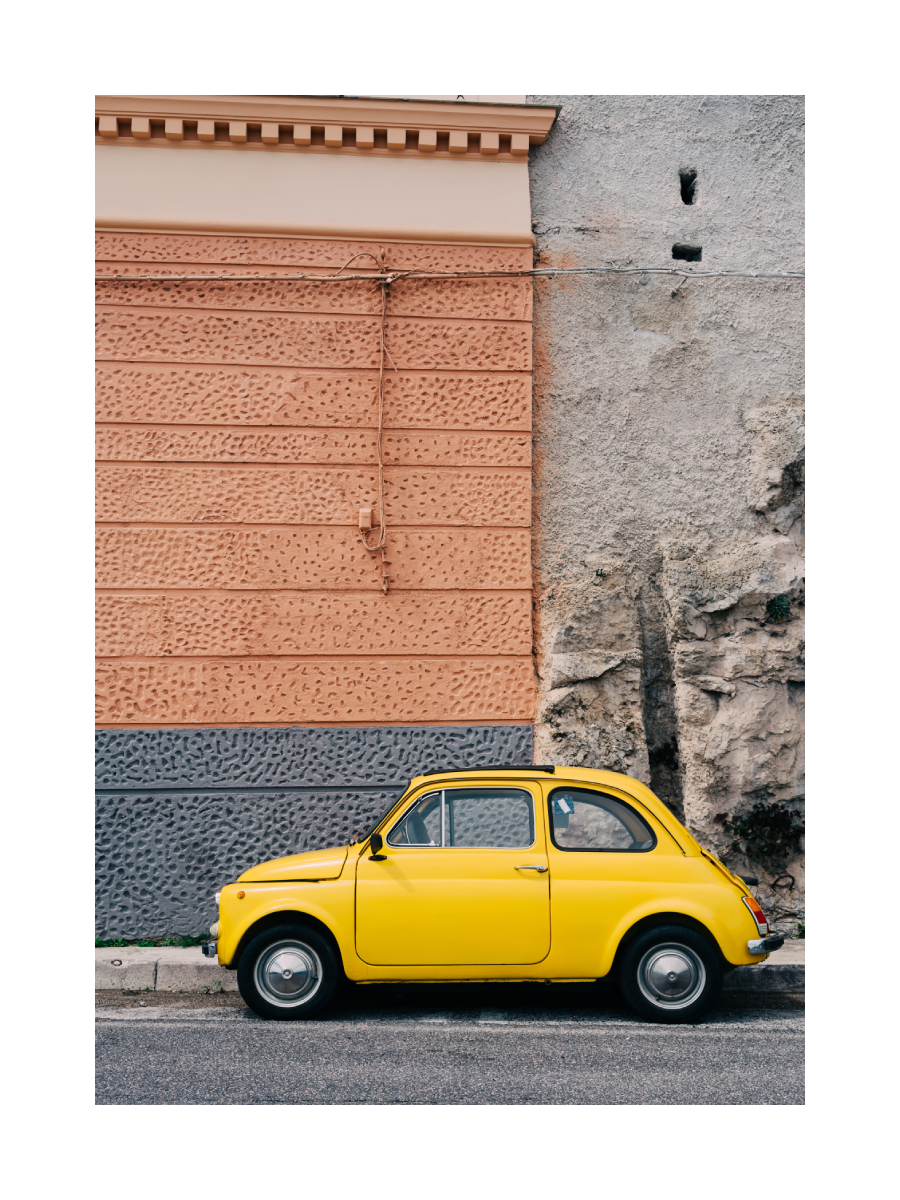 Fotografie eines gelben Autos vor einer orangefarbenen Wand.