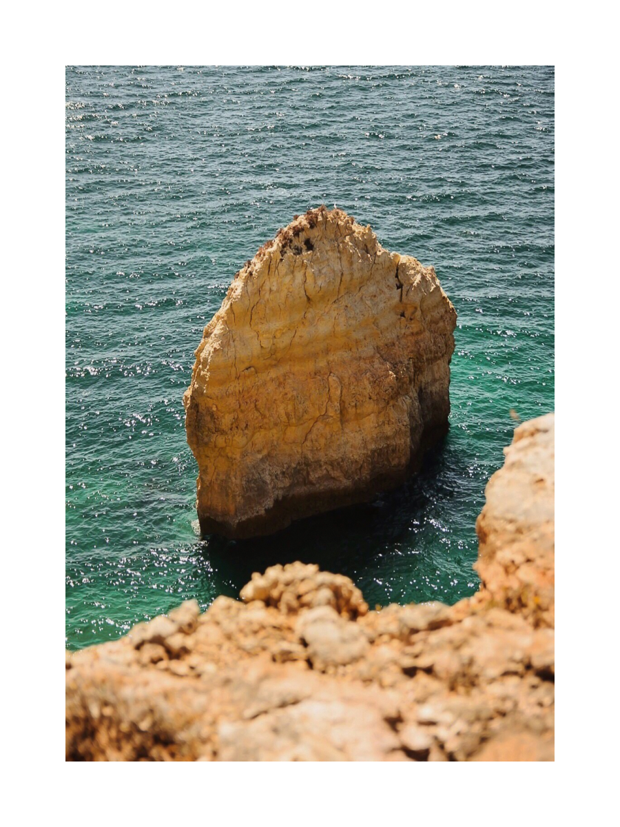 Fotografie eines großen gelben Felsens im türkisfarbenen Meer.