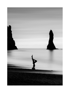 Schwarz-weiß-Fotografie einer Frau im Kopfstand am Strand mit Felsen im Hintergrund.