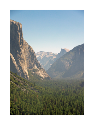 Fotografie des Yosemite Valley mit grünen Bäumen und blauen Bergen im Hintergrund.