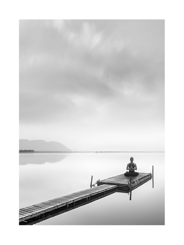 Schwarzweiß-Fotografie einer Frau, die auf einem Steg im Lotussitz meditiert, umgeben von Wasser und bewölktem Himmel.