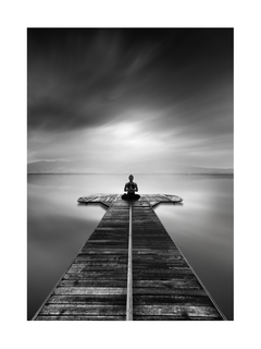 Schwarz-weiß-Fotografie einer Frau, die auf einem Steg in einem See meditiert.